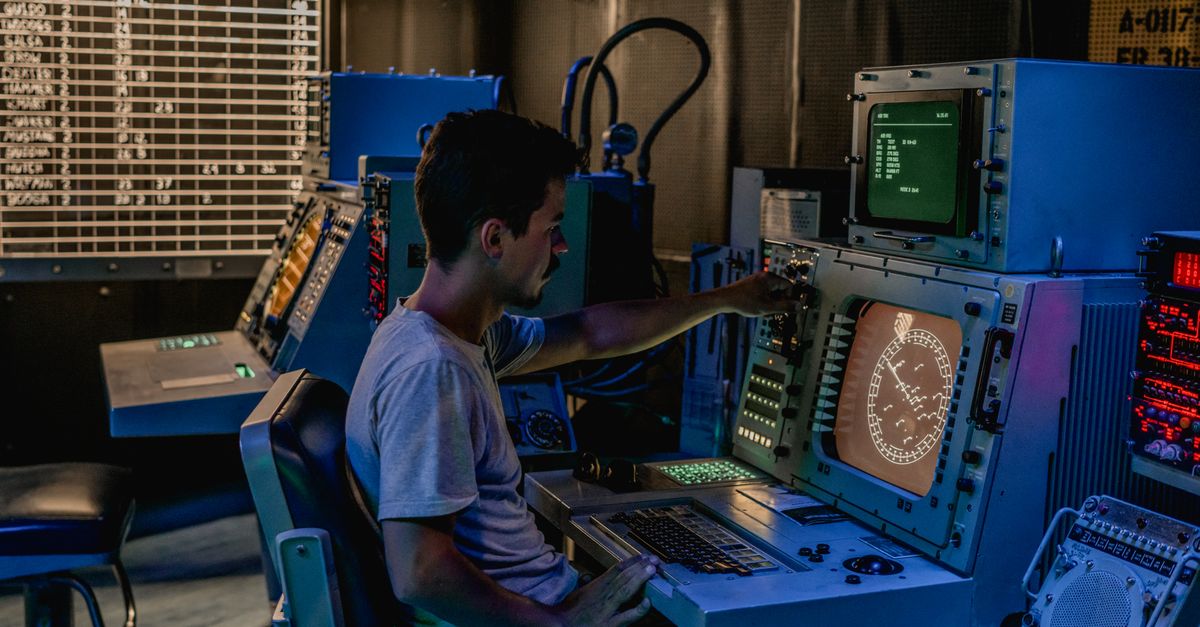 Persona revisando paneles de control en una sala con iluminación tenue